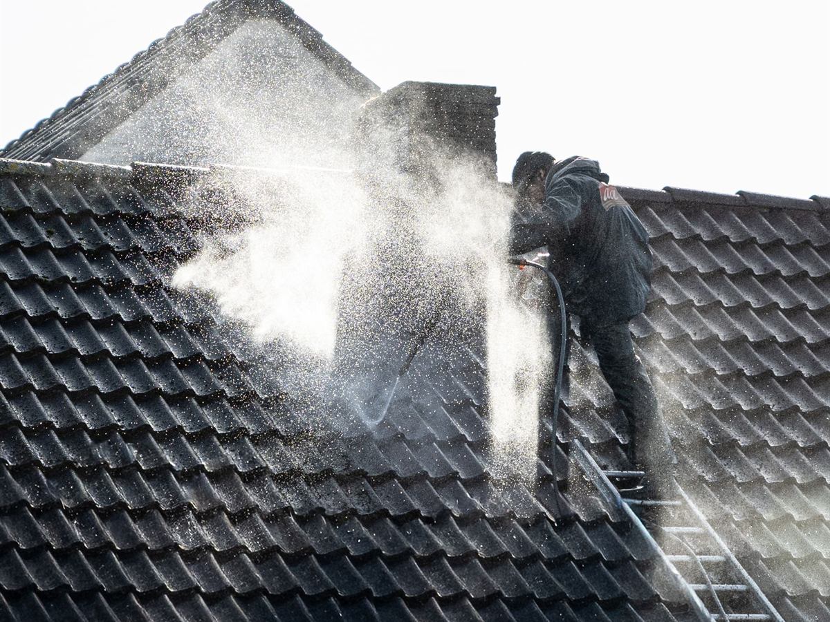 Couvreur sur une échelle nettoyant une toiture en tuiles au nettoyeur haute pression